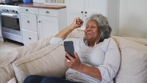 senior african american woman wearing earphones having a video call on smartphone at home