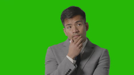 portrait of serious businessman in suit thinking against green screen having idea