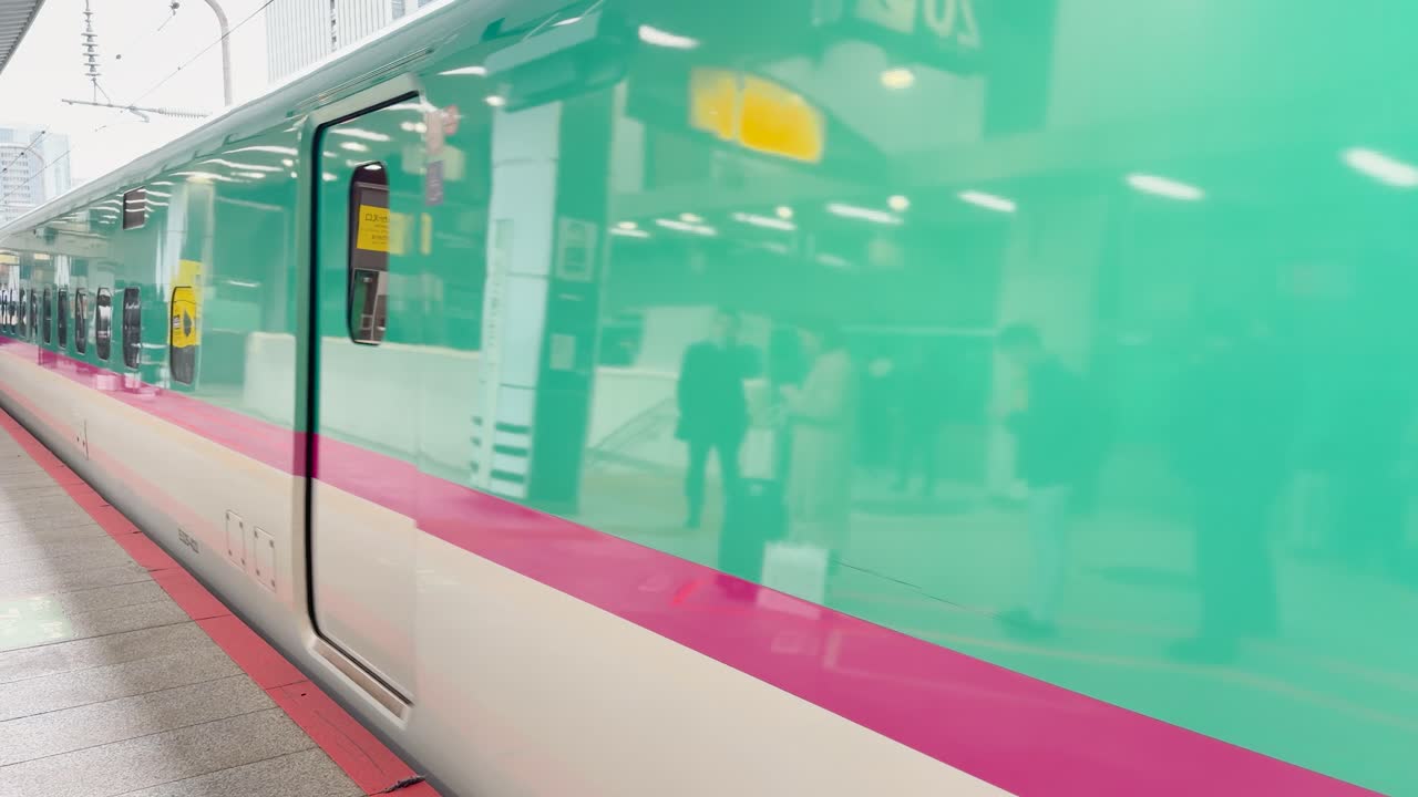 日本の東京の駅のホームに、ティールとピンクの新幹線が滑り込む。