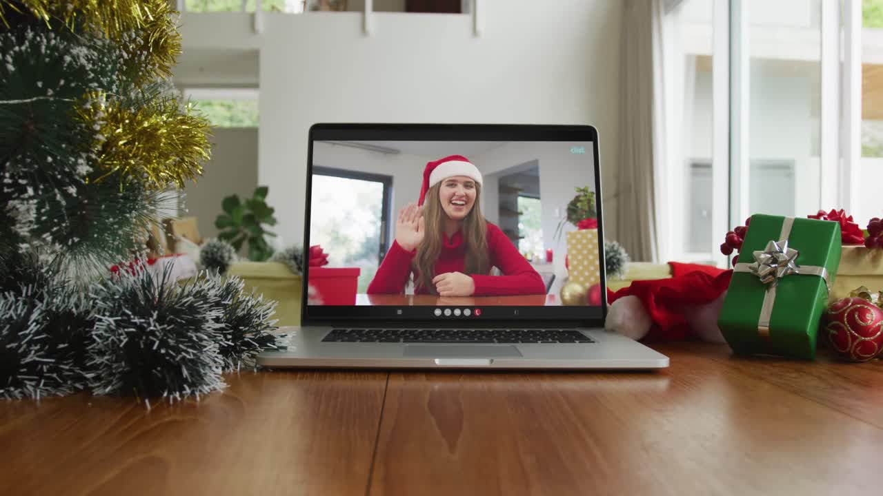 mujer caucásica sonriente con sombrero de papá noel y saludando en la videollamada de navidad en la computadora portátil