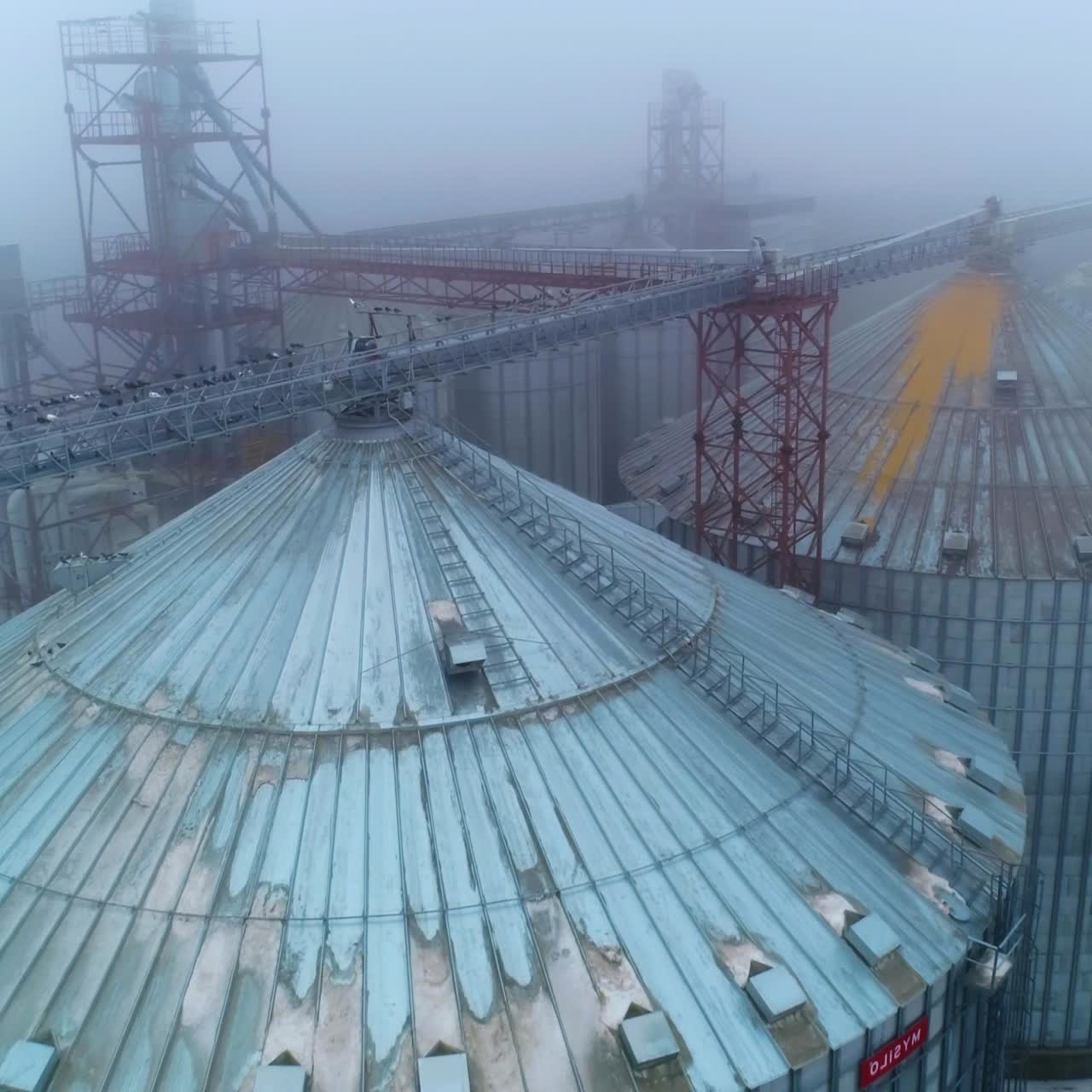 Huge tanks of grain processing plant. View on the tops of elevator reservoirs in mist. Aerial perspective