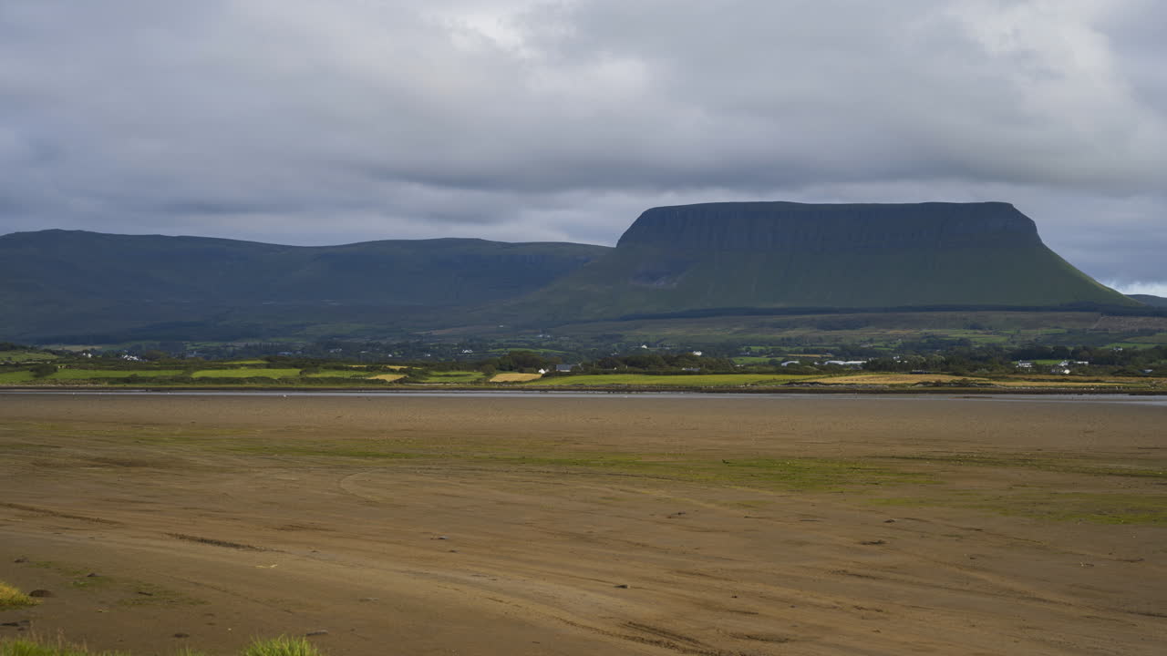 lapso de tiempo de la costa del mar de arena de irlanda con colinas en la distancia y nubes en movimiento en el cielo