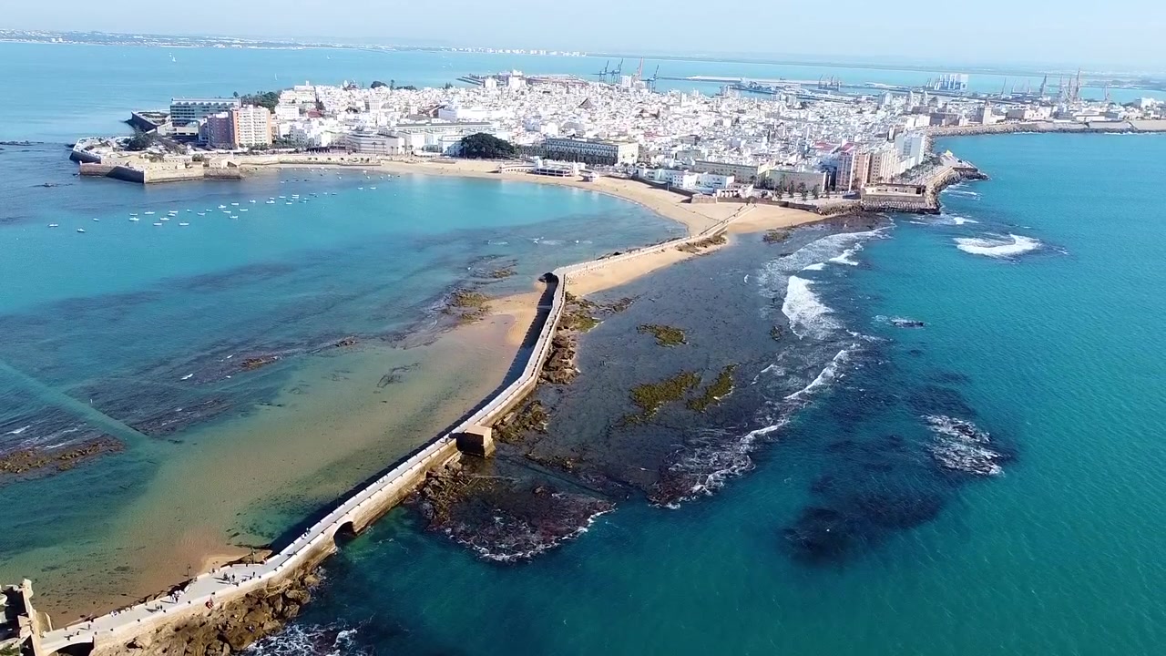 Cadice. Spiaggia La Caleta. Spagna. Vista aerea della spiaggia, del frangiflutti e delle barche da pesca ancorate in una cala di un mare turchese splendente.