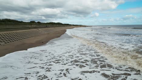 Typical-English-seaside-resort,-shot-using-a-fast-moving-drone,-giving-a-high-aerial-viewpoint-showing-a-wide-expanse-of-sandy-beach-with-a-pier-and-crashing-waves