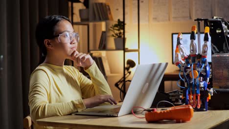 teen asian girl thinking while working about a cyborg hand on a laptop at home