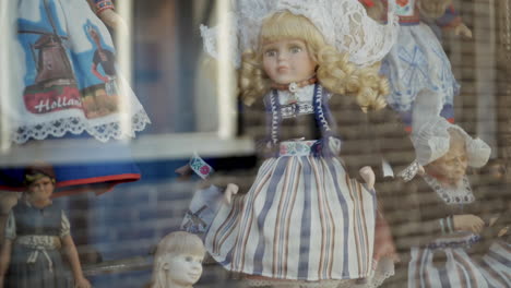 rag doll toy baby with iconic dutch clothes, rotating on turntable, showcasing at shop display window of city store in slowmo