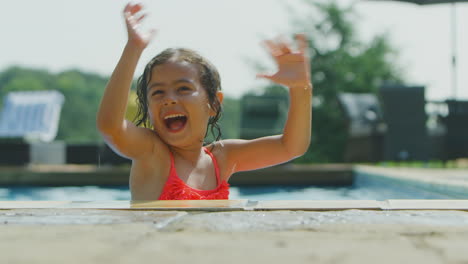 Portrait-Of-Young-Girl-Looking-Over-Edge-Of-Outdoor-Pool-On-Vacation