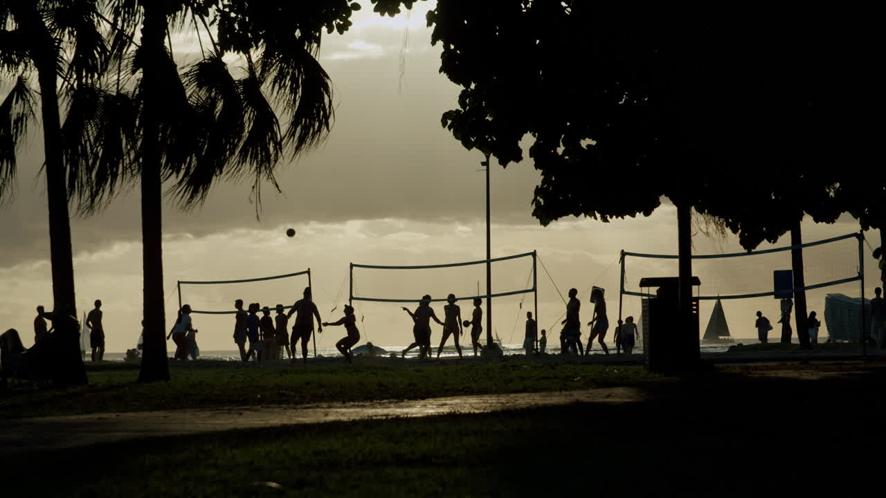 Silhouettes of people playing beach volleyball at sunset