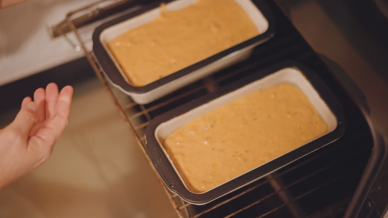 To gresskarbrød er plassert i ovnen, i rektangulære former på risten, mens en forsiktig baker skyver inn brettet. Den varme krydderaromaen antyder et dobbelt parti med brød til høytidsgodt, en del av en effektiv kjøkkenrutine.