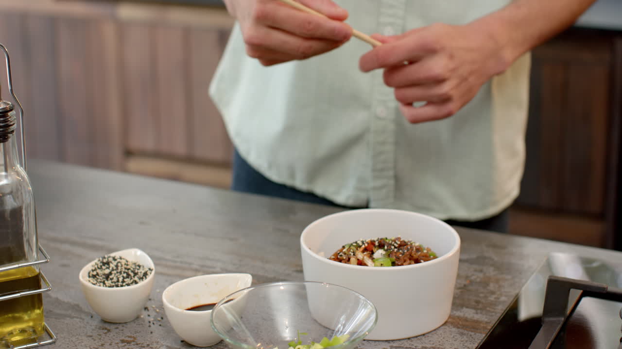 Asian man enjoying meal with chopsticks in modern kitchen at home