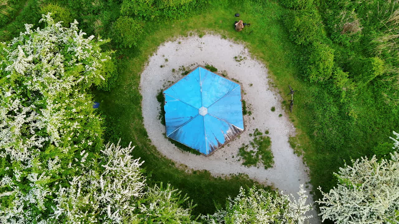 Rising over the blue roof of gazebo in the green nature. Blossoming trees grow around the lawn.