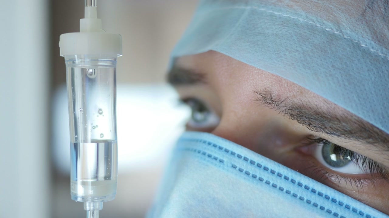 Primo piano di flebo con medico in mascherina chirurgica che monitora