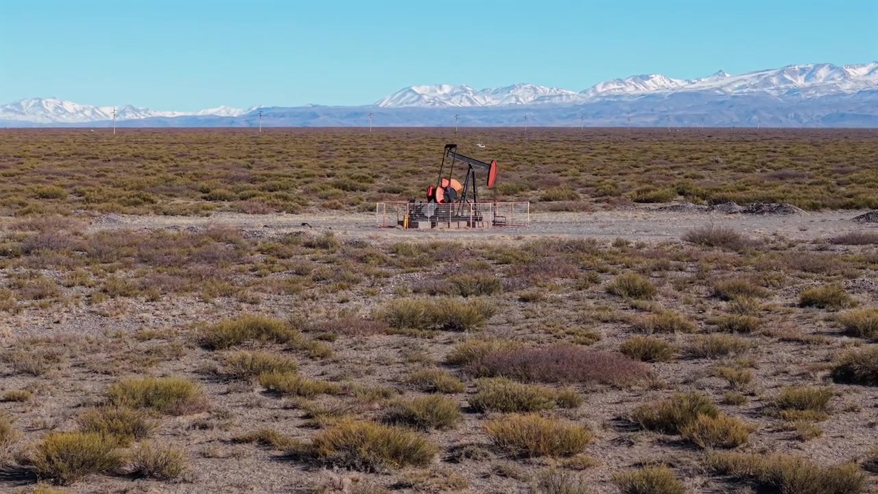 Oil pumpjack on arid plain near Malargue with snowy Andes mountains beyond, aerial descend approach, parallax with ridgeline