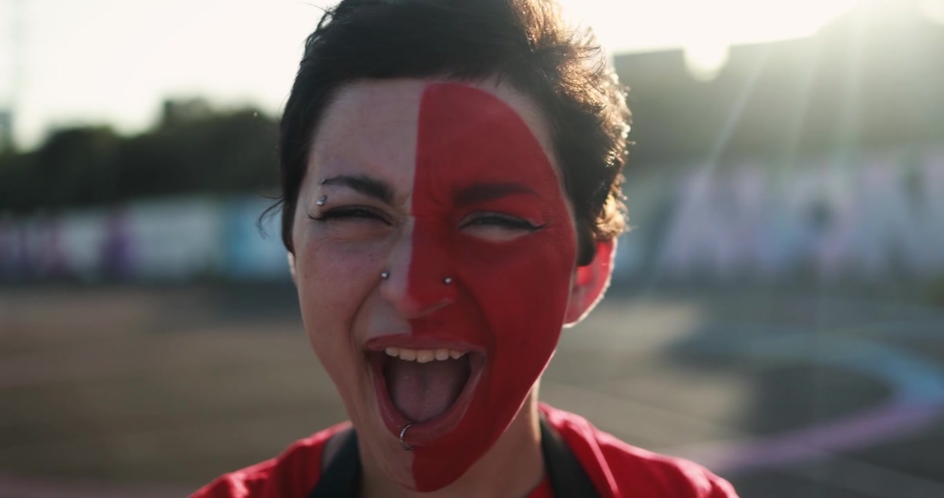 Giovane donna con il viso dipinto di rosso che urla per l'emozione