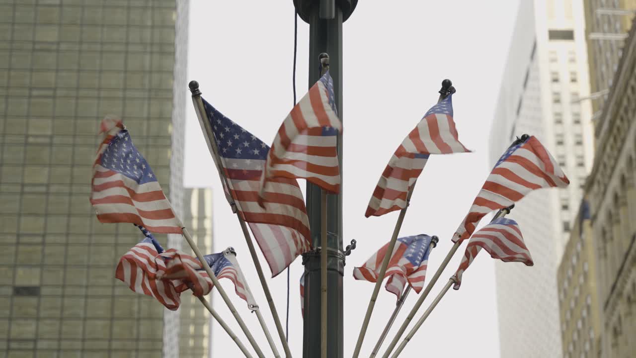 Close-up shot of a bunch of US flags fluttering on a pole in New York City, capturing the patriotic symbols against the urban backdrop.