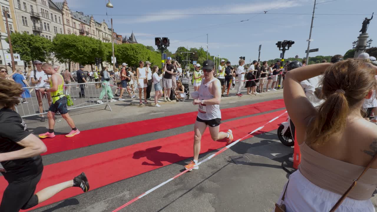 Runners compete in Stockholm Marathon on sunny day with crowd cheering near red carpet finish