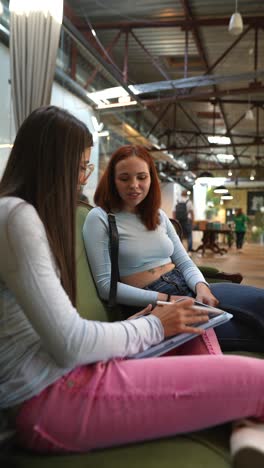 dos mujeres colaborando en un proyecto digital en un espacio industrial moderno