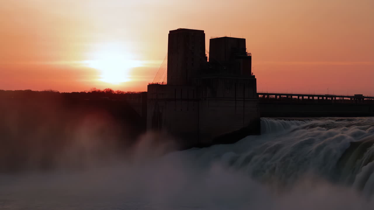 Sunset Silhouetting a Hydroelectric Power Plant and Waterfall