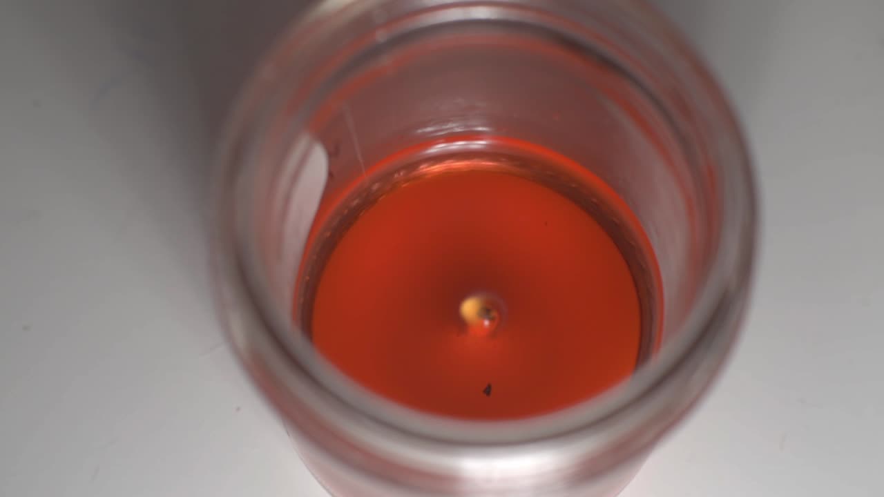 Little Flame Burning On A Red Candle Melting In A Glass - top shot