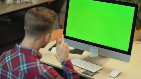 Young-man-call-video-online-on-computer-with-green-screen-in-office
