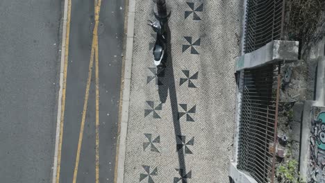 Art-decorated-sidewalk-with-two-column-triangular-patterns-and-a-motorbike-parked-beside-the-lamp-post