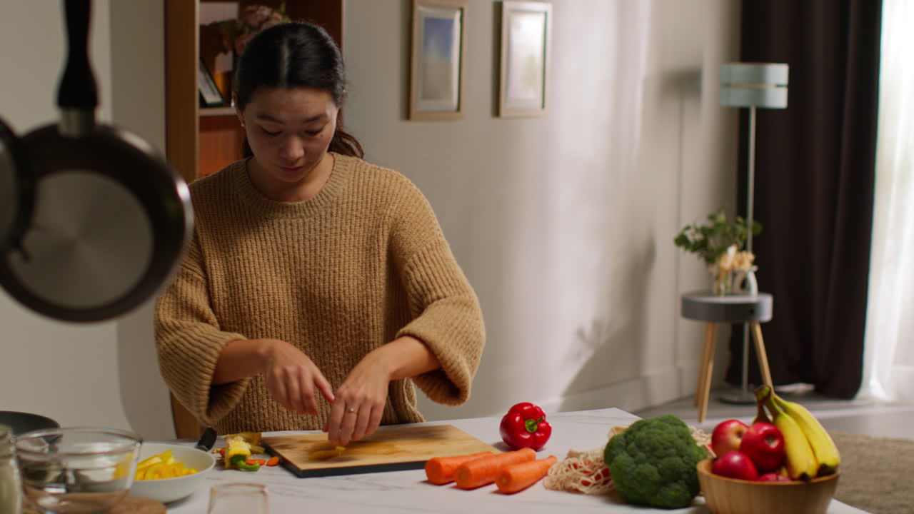 가정에서 부에 있는 여성이 채식주의자 또는 채식주의자의 식사로 건강한 신선한 채소를 준비하고 은색과 노란색 고추를 조각하고 있습니다.