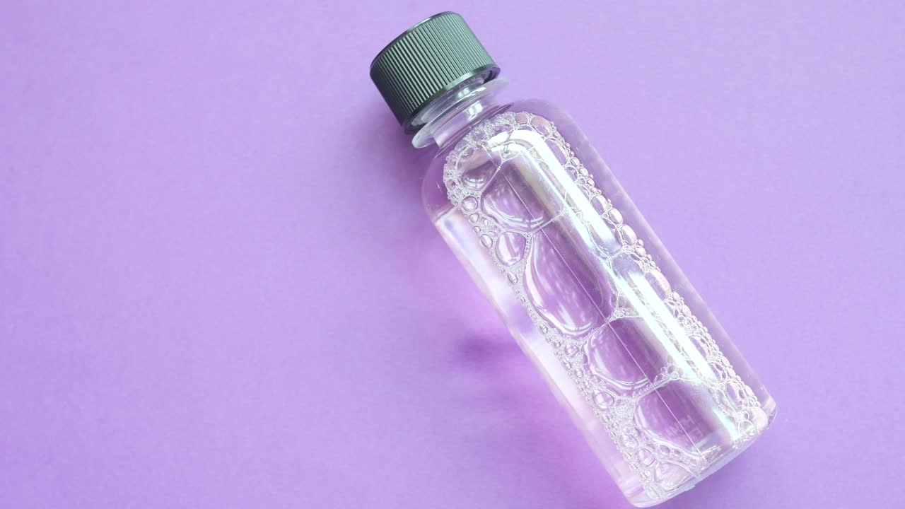 pequeña botella de líquido transparente con burbujas en fondo púrpura