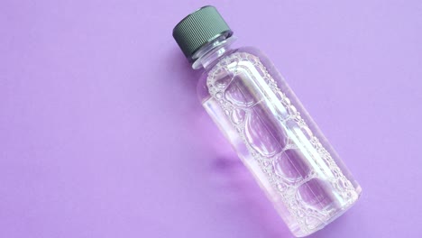 pequeña botella de líquido transparente con burbujas en fondo púrpura
