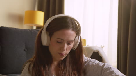 woman wearing wireless headphones sitting on floor at home streaming music from mobile phone 7