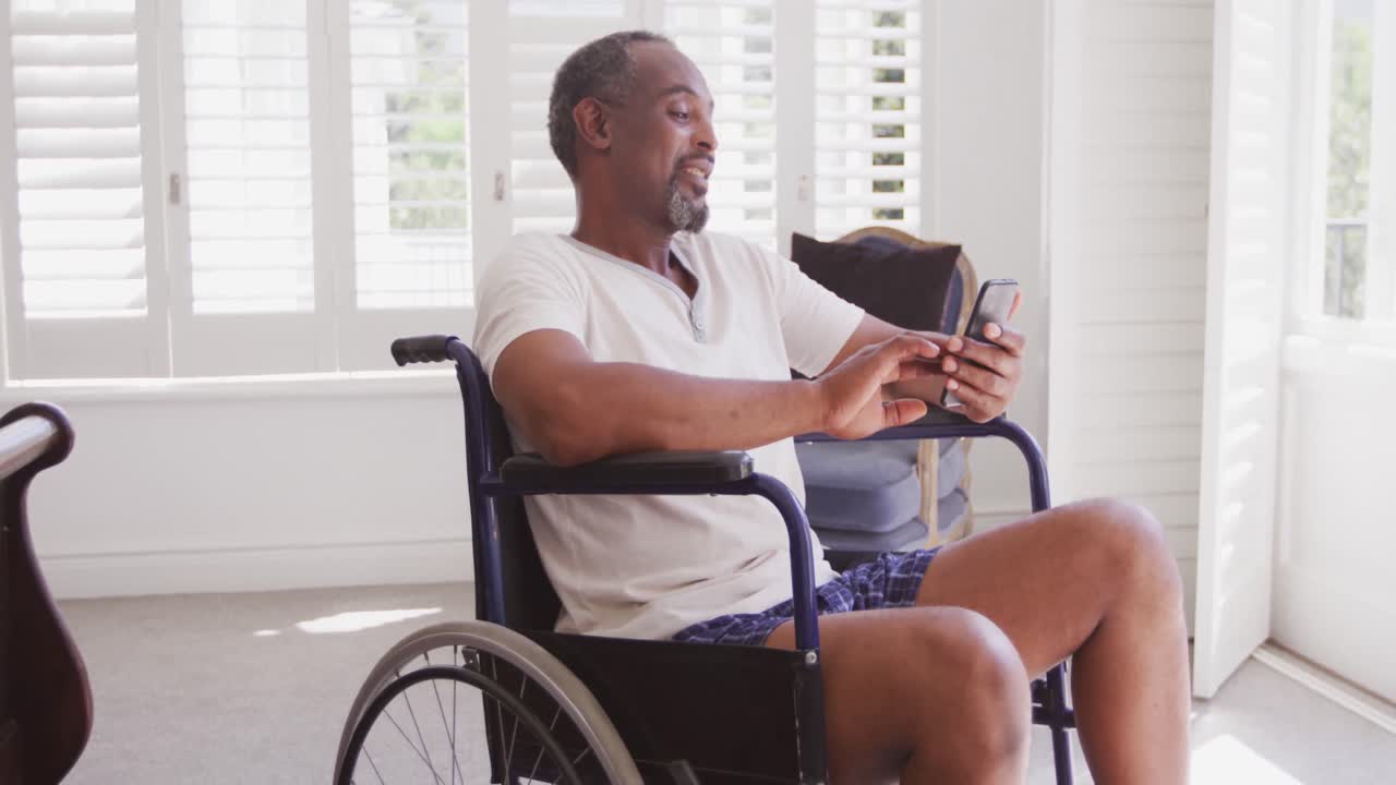 Senior African American man on a wheelchair, using his phone, smiling at home
