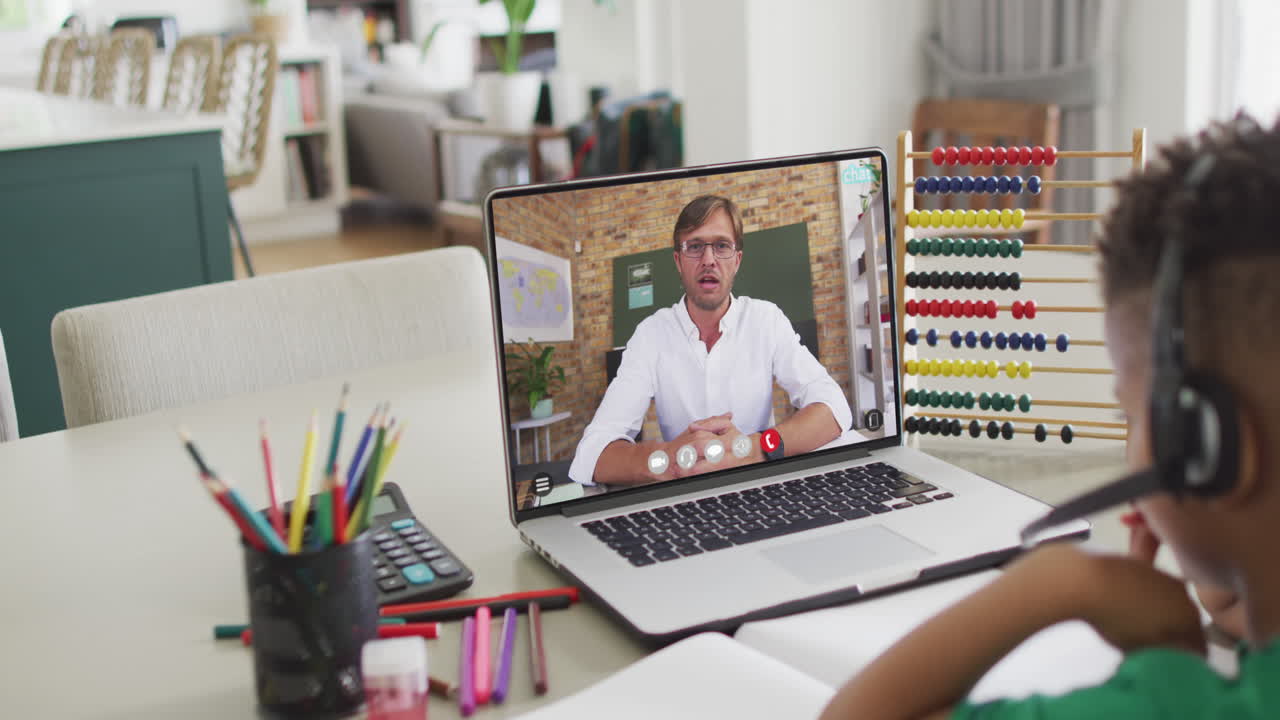 Diverse schoolboy having laptop video call with male teacher in slow motion
