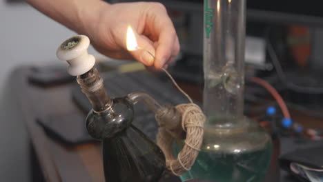 hemp wick around the base of a bong is lit and held to a bowl of cannabis