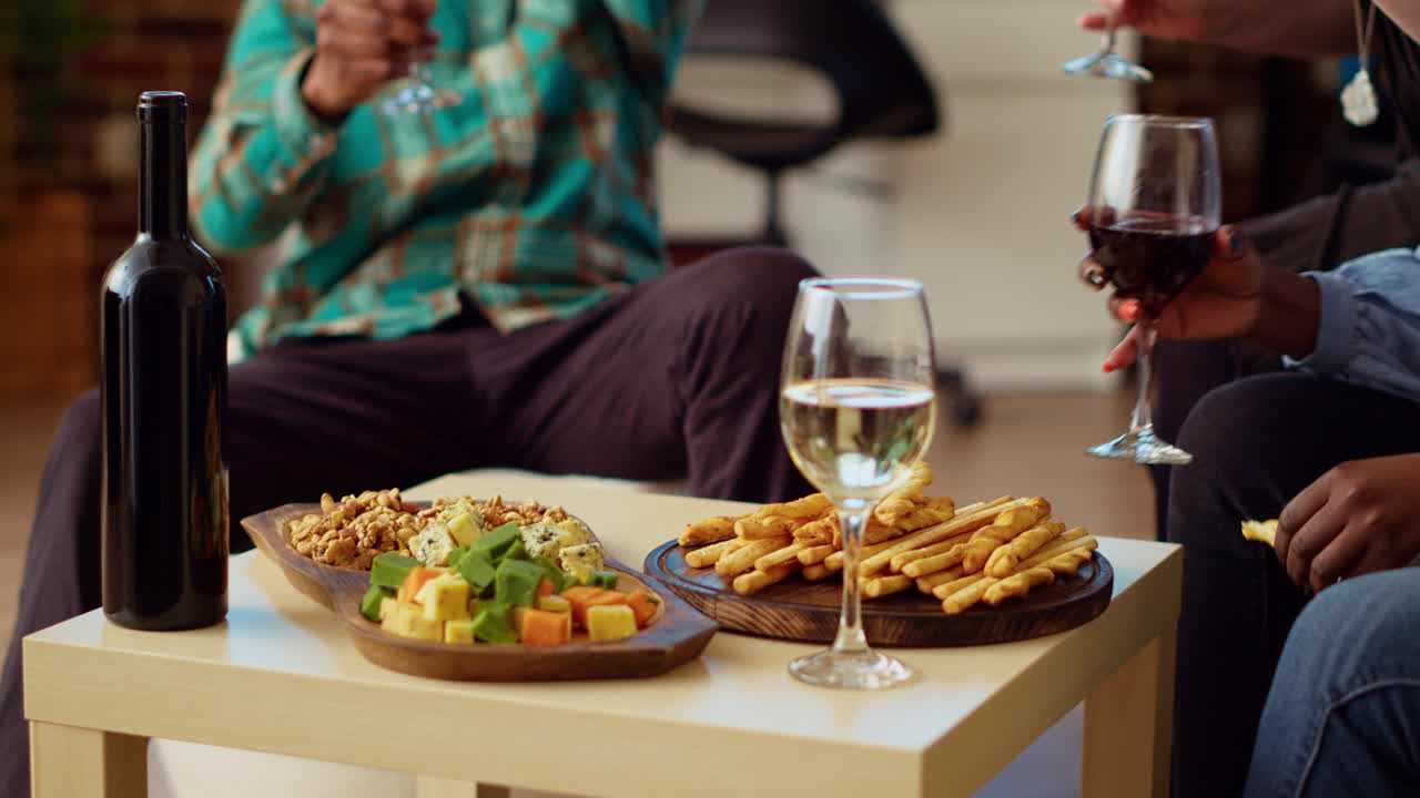 Close up shot of charcuterie board on stylish living room table next to group of friends talking