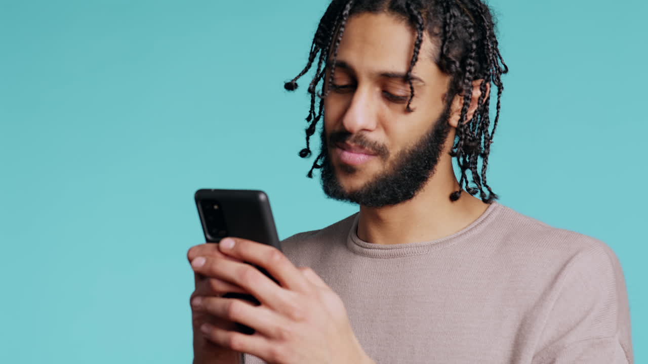 Uomo che invia messaggi a un amico usando lo smartphone, ridendo per una battuta divertente, su sfondo studio.