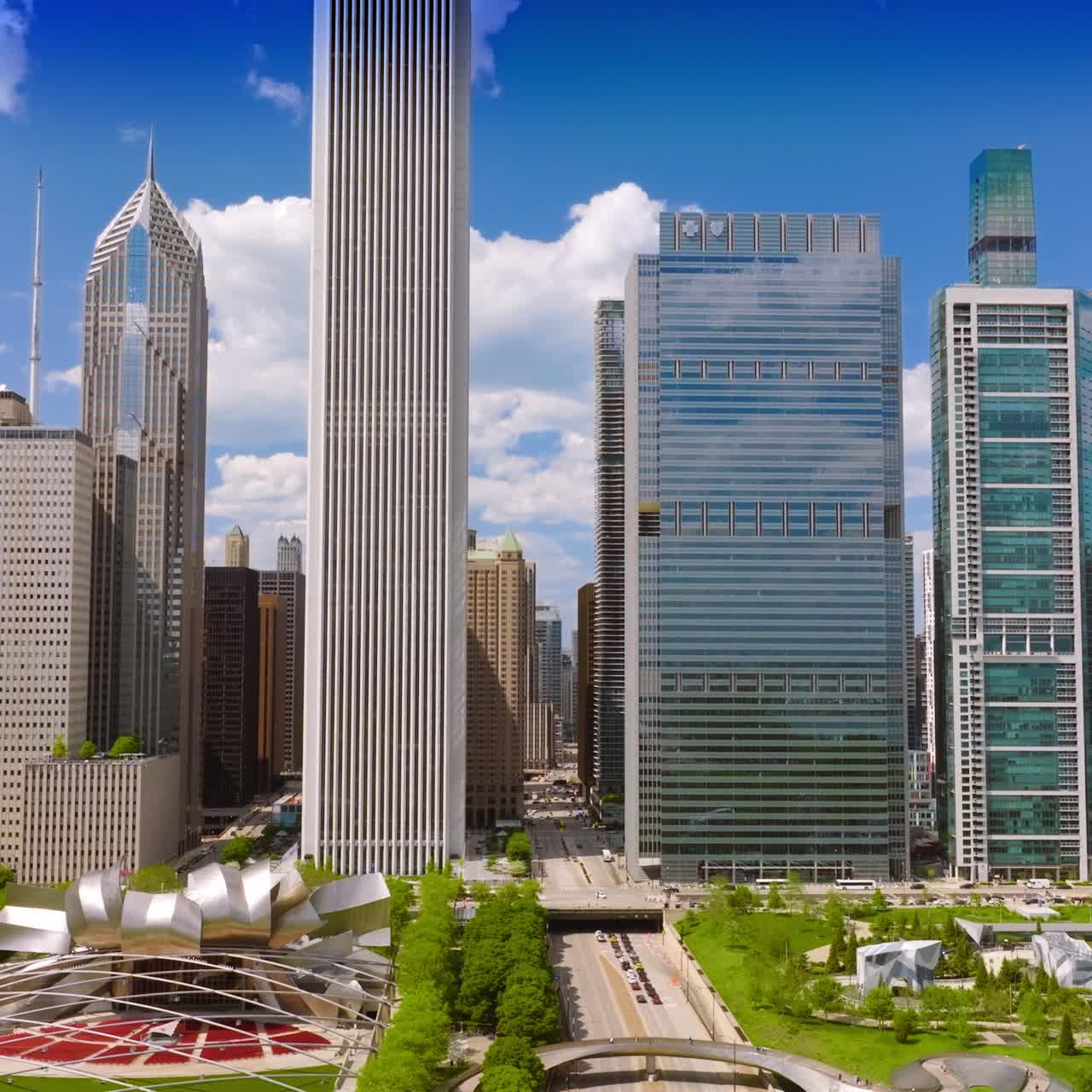 Wide road going through the famous Millennium Park in downtown Chicago. Greenery and metal installations at the backdrop of modern architecture