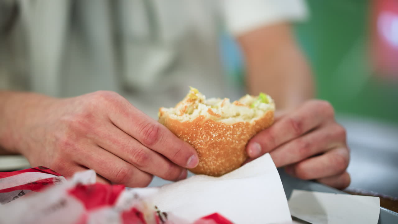 Front view of two hands holding greasy snack with oil shine on fingers, closeup showing texture and crumbs, blurred background suggesting casual eating moment, expression of enjoyment and craving