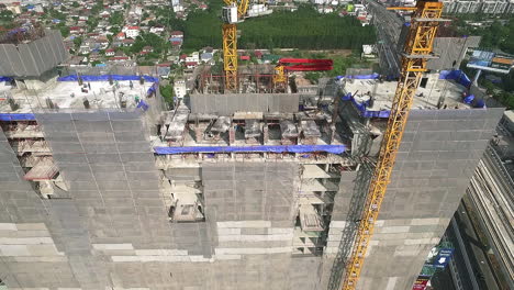 Aerial-view-of-modern-high-rise-building-under-construction-in-the-busy-city-centre-business-district-with-workers,-scaffolding-and-crane