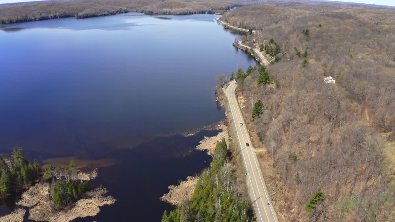 Drone shot of cars travelling on rural Ontario highway beside lake