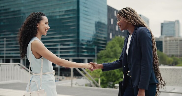 Two Businesswomen Shaking Hands and Talking Outside Modern Office Building