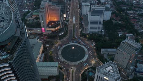 aerial tilting horizontal to overhead view of a busy traffic on a selamat datang monument roundabout surrounded by modern skyscrapers in jakarta, indonesia