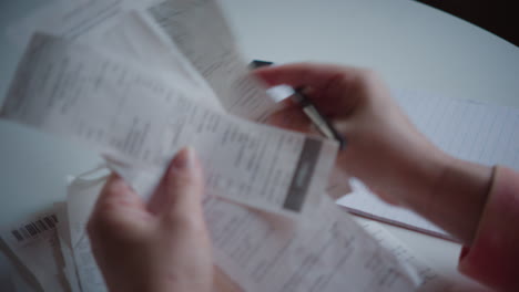 personal finance and organization, female right hand tracks through receipts, writing down budget and numbers in notepad on desk