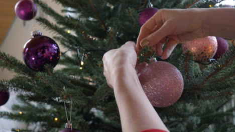 closeup of a pair of hands putting an ornament on a christmas tree