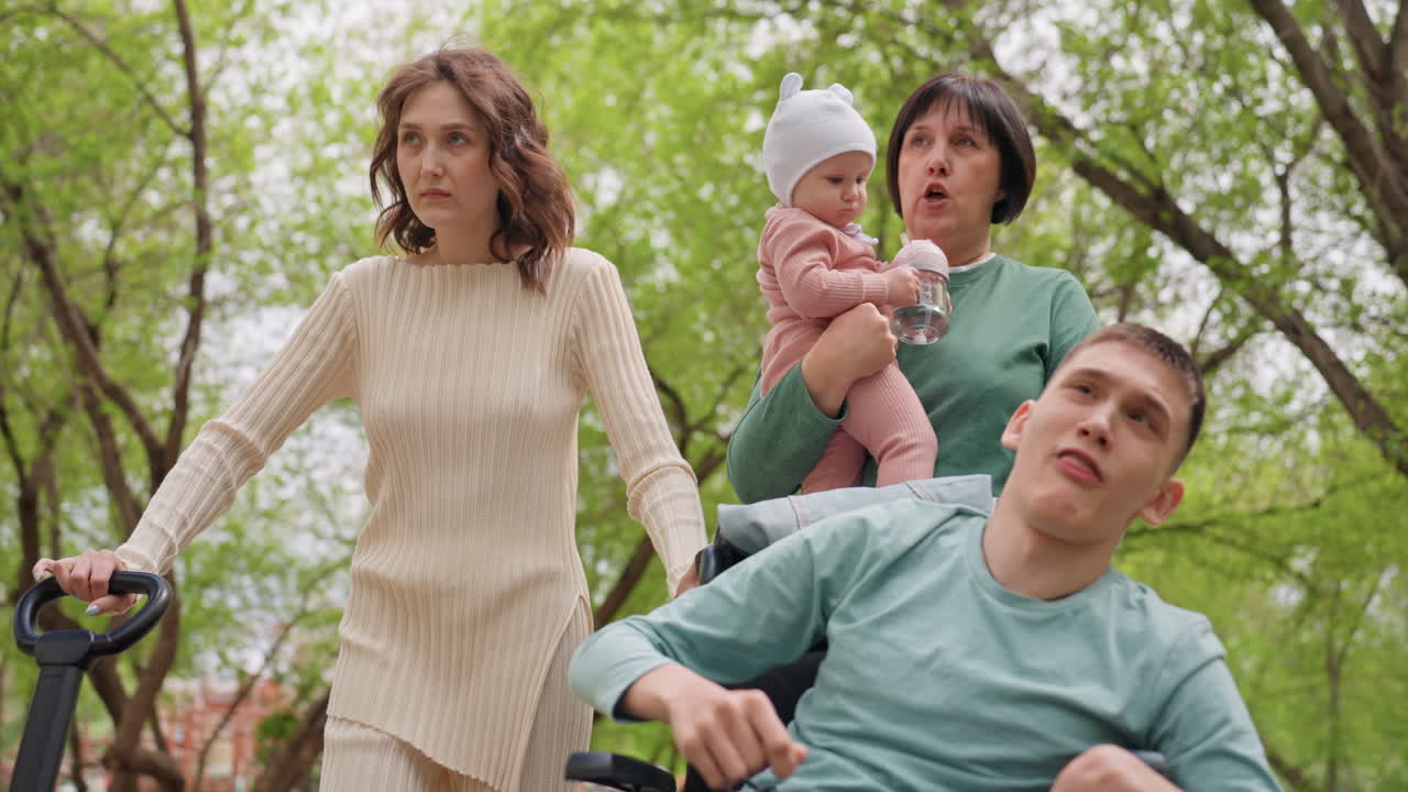 Woman Pushing Wheelchair With Family Outdoors, Companion Holding Infant While Caregiver Guides Wheelchair User Along TreeLined Path, Warm Spring Light And Gentle Breeze, Supportive Expressions