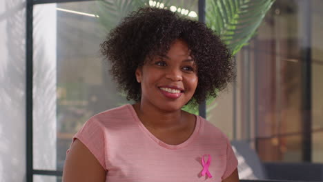 smiling woman wearing pink breast cancer awareness ribbon talking at meeting of therapy support group for cancer treatment patients 3