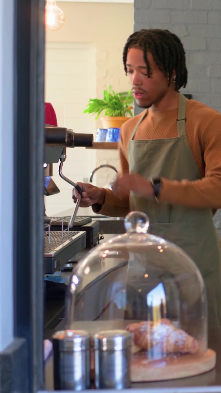 Video verticale: Consegna di tazza e scatola, cliente che lascia il bancone, barista in grembiule che vaporizza l'espresso.