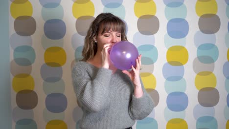 mujer joven que sopla un globo púrpura frente a un fondo colorido