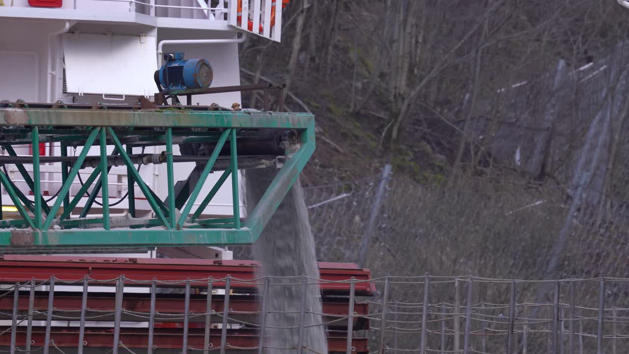 선박의 화물창에 모래를 대량으로 적재하는 컨베이어 벨트 - 화물창으로 떨어지는 아노소사이트 재료가 있는 벨트의 근접 촬영 - 구드반겐 노르웨이