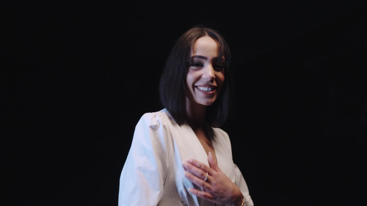 beautiful woman laughing in slowmotion. she wears a white dress. dark background.