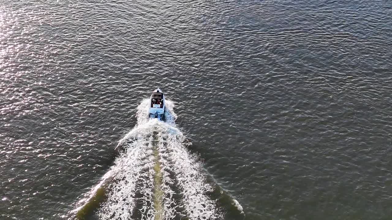 Aerial view of a speedboat creating a wake as it moves swiftly across a wide river.