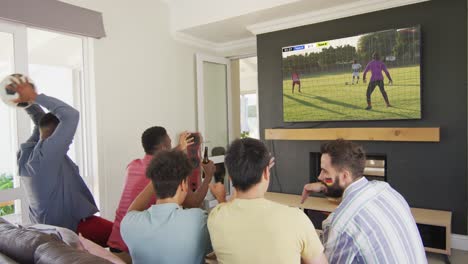 Video-Von-Verschiedenen-Freunden,-Die-Auf-Dem-Sofa-Sitzen-Und-Zu-Hause-Fußball-Im-Fernsehen-Schauen